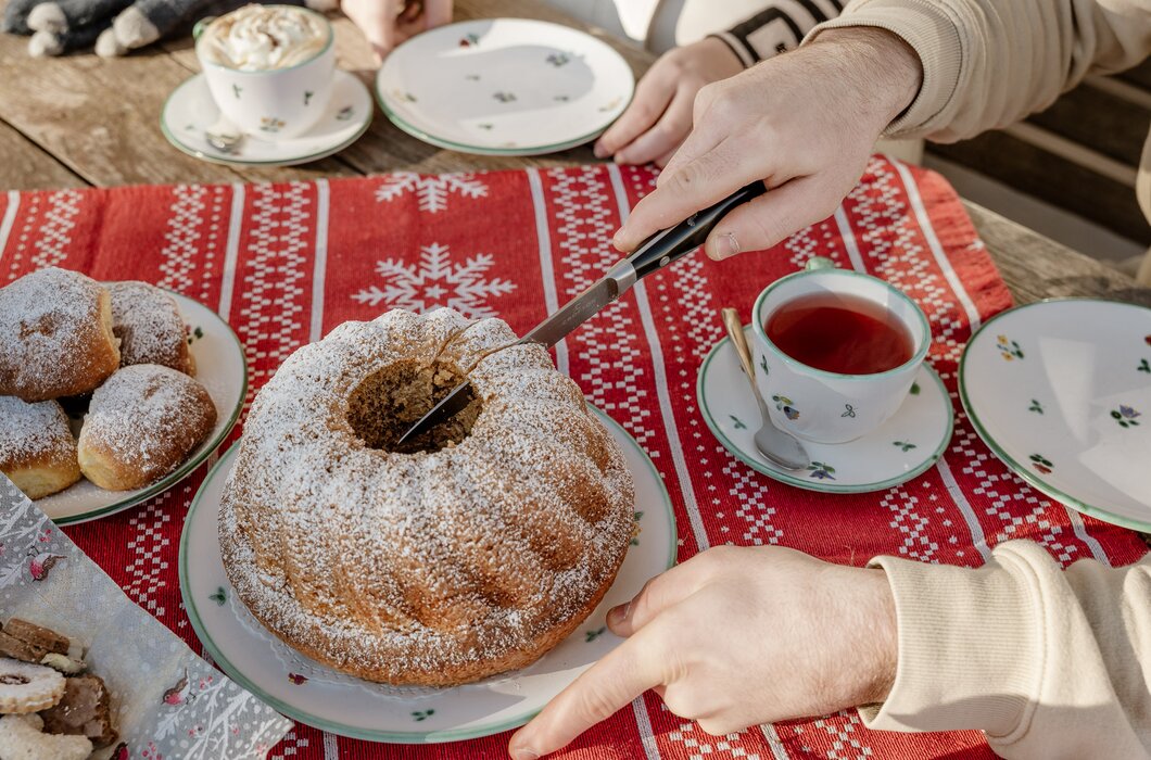 Eine Kaffeepause im Freien vor dem Bauernhaus. Ein Mann schneidet einen Gugelhupf an. Drum herum stehen Kaffeetassen und Teller.  | © UaB Steiermark / Wolfgang Spekner