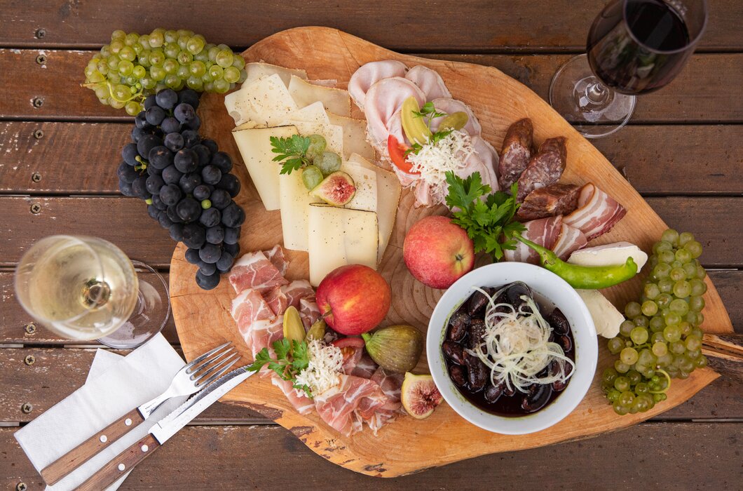 Eine herzhafte steirische Brettljause am Holzbrett serviert, mit Würsteln, Speck, Rohschinken, Käse, Weintrauben, Äpfeln, frischen Feigen und Käferbohnensalat | © Urlaub am Bauernhof / punkt & komma