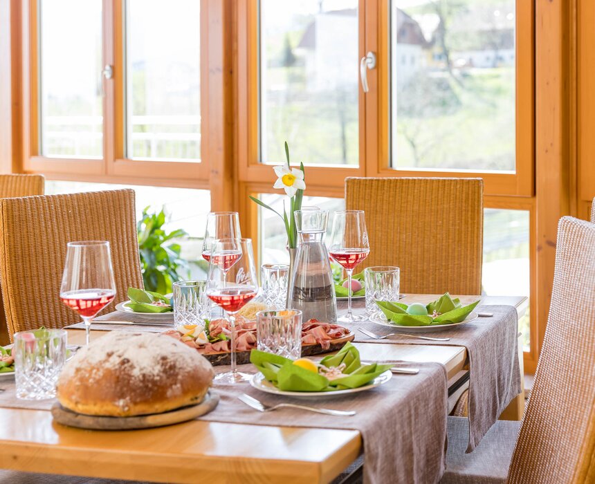 Ein gedeckter Tisch mit einer Osterjause, Frühlingsdekoration und vier Gläsern Wein. | © Urlaub am Winzerhof / ELISABETH FRÖHLICH photography
