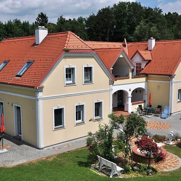 Der Bauernhof von außen, mit Garten und mehreren Terrassenbereichen mit Sitzgelegenheiten.
