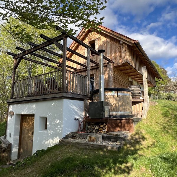 Die Außenansicht des Bauernhofs mit Holzbalkon, einer Pergola und einem holzbefeuerten Badezuber.