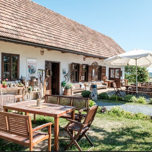 Der Außenbereich des Hofs bietet Holztische, Bänke und Sonnenschirme vor der weißen Fassade mit roten Dachziegeln.