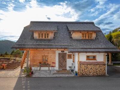 Außenansicht des Ferienhauses mit Holzfassade, weiß verputzten Wänden, Schindeldach, einer Terrasse mit Sitzgelegenheiten und einem Holzstapel.