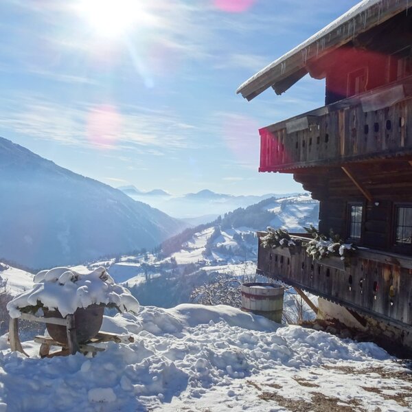 Die verschneite Alm von außen mit Balkonen und Weitblick über die winterliche Landschaft.