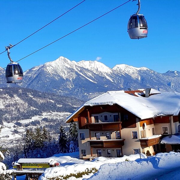 Das Aparthotel & Restaurant Ederhof im Winter, direkt an der Skipiste gelegen, mit vorbeifahrenden Gondeln und Bergblick.