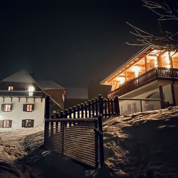 Außenansicht des Ferienhauses bei Nacht, mit Schnee und hell erleuchteten Fenstern und Balkonen.