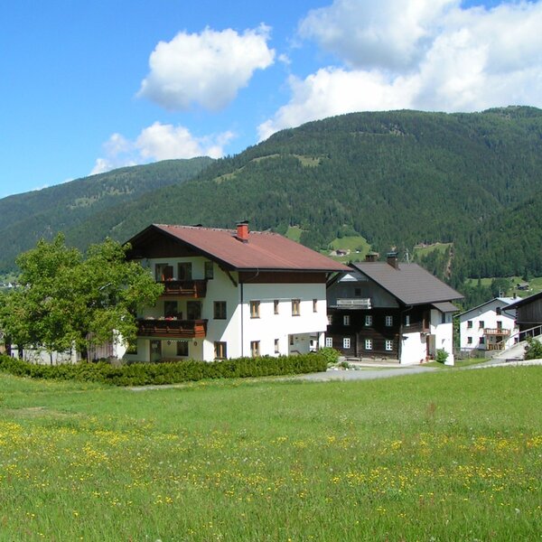 Das Gebäude des Bauernhofs mit Balkonen, umgeben von grünen Wiesen und Bergpanorama.
