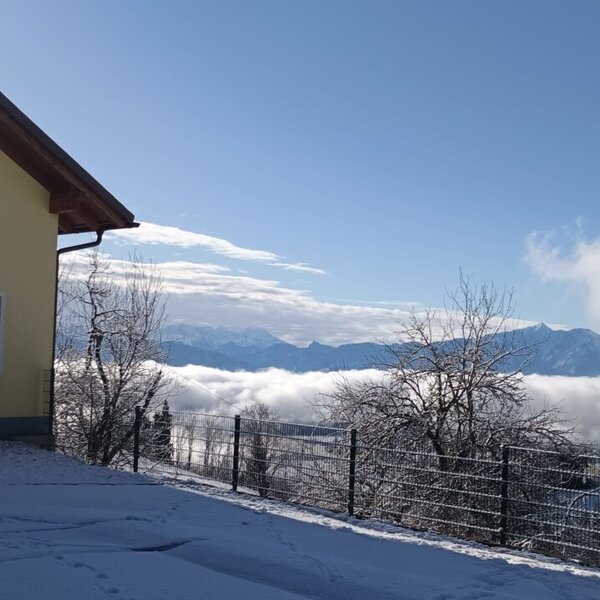 The Farm House exterior, with a snow-covered driveway, overlooks distant mountains and valleys covered in clouds.