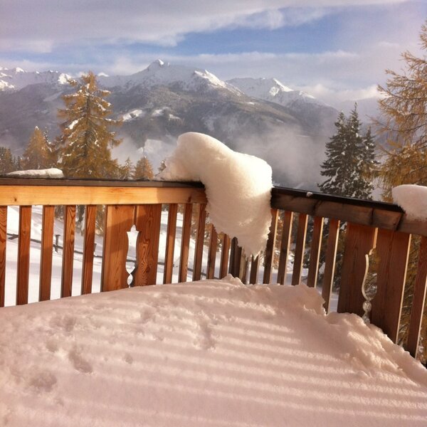 Die schneebedeckte Terrasse der Alm mit Holzgeländer und Ausblick auf die verschneiten Berge.