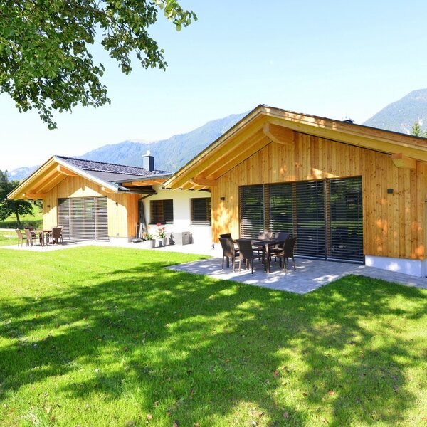 Außenansicht des Bauernhofs mit zwei Gebäuden, möblierten Terrassen und umliegendem Garten mit Bergblick.