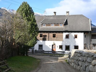 Außenansicht der Ferienwohnung mit weiß getünchten Wänden, Holzverkleidung und einem Zufahrtsweg.