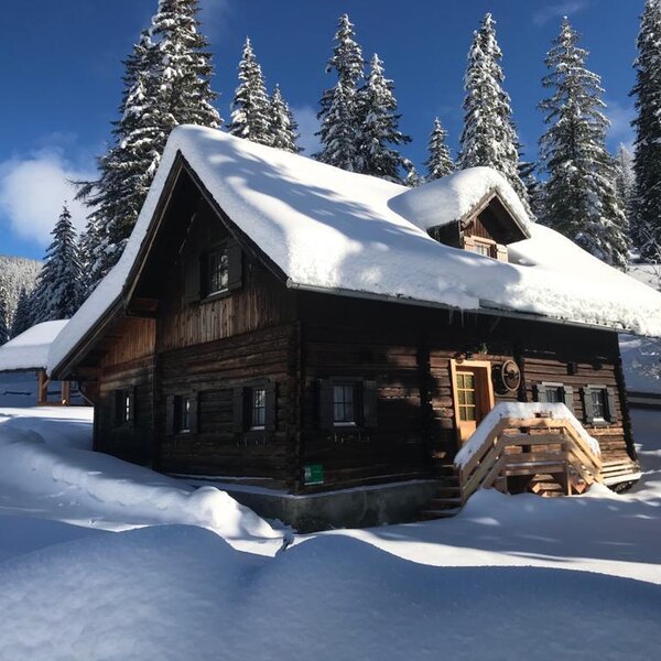 Die Alm, umgeben von tiefem Schnee und schneebedeckten Nadelbäumen im Winter.
