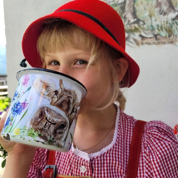 A child in traditional attire drinks from a cow-themed mug at the Farm House.