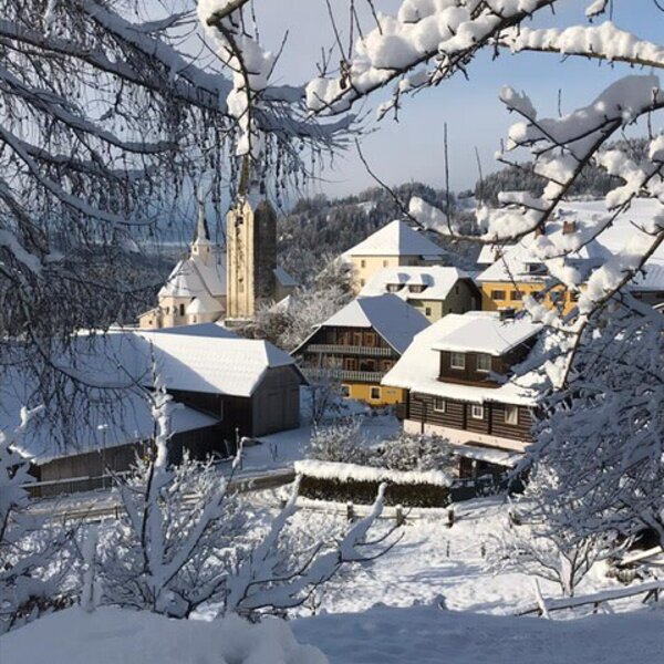 A winter view of the village, showcasing snow-covered houses and a church steeple.