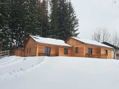 Langhanshütten in verschneiter Landschaft, umgeben von Tannenbäumen.