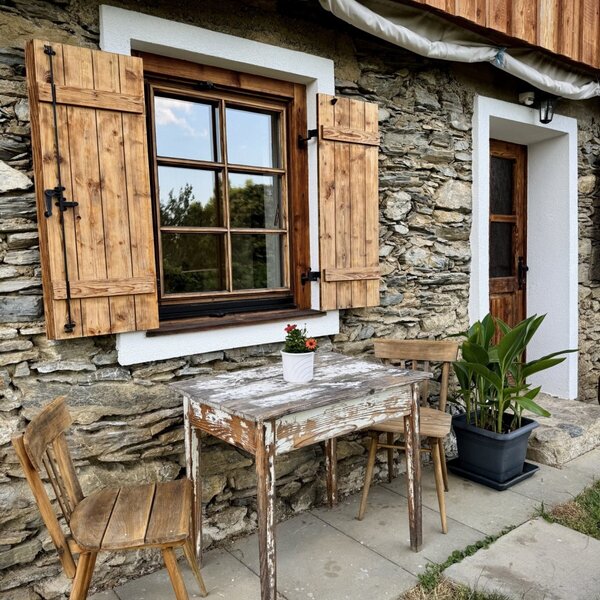 Außenbereich des Bauernhofs mit Steinfassade, Holzfensterläden und Sitzgelegenheiten.