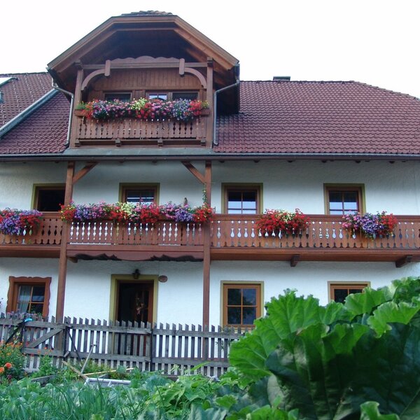 The Farm House features a white exterior with two levels of wooden balconies adorned with colorful flower boxes, overlooking a fenced garden area.