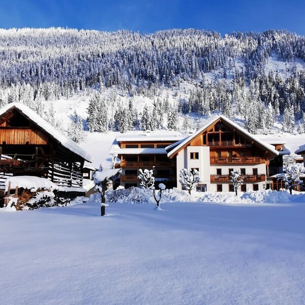 The Farm House property in winter, featuring the main building and a traditional wooden barn, surrounded by snow with a forested mountain in the background.