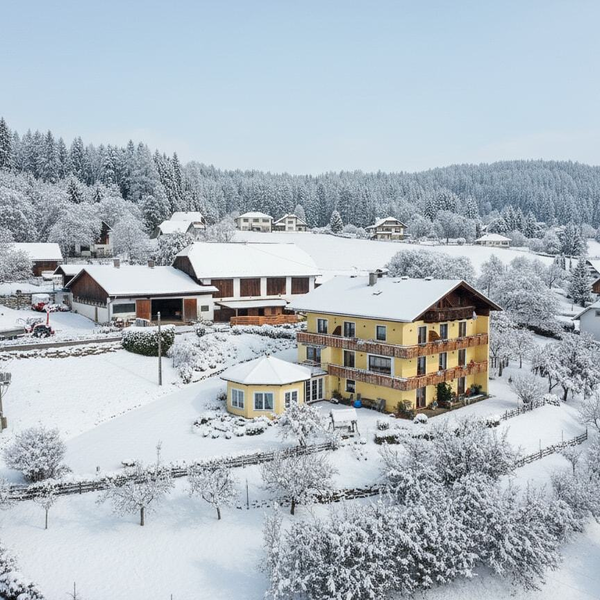 Der Bauernhof im Winter, umgeben von schneebedeckten Feldern und Wäldern.