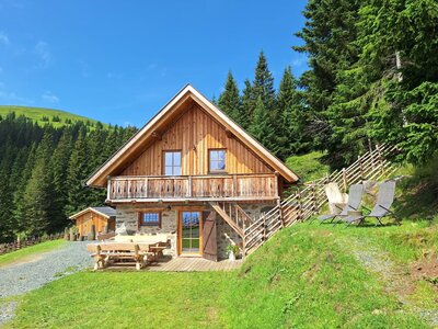 Gemütliche Berghütte mit Sitzgelegenheiten im Freien und Liegestühlen auf einer grünen Wiese. Gemütliche Berghütte mit Sitzgelegenheiten im Freien und Liegestühlen auf einer grünen Wiese.