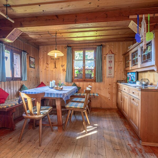 The Alpine Hut features a dining area with a wooden table, bench seating, and an integrated kitchen with wooden cabinets and a sink.