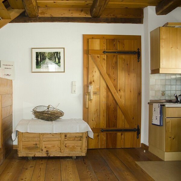 An interior view of the vacation rental, featuring a wooden door, a partial kitchen, a wooden chest, and exposed wooden beams.