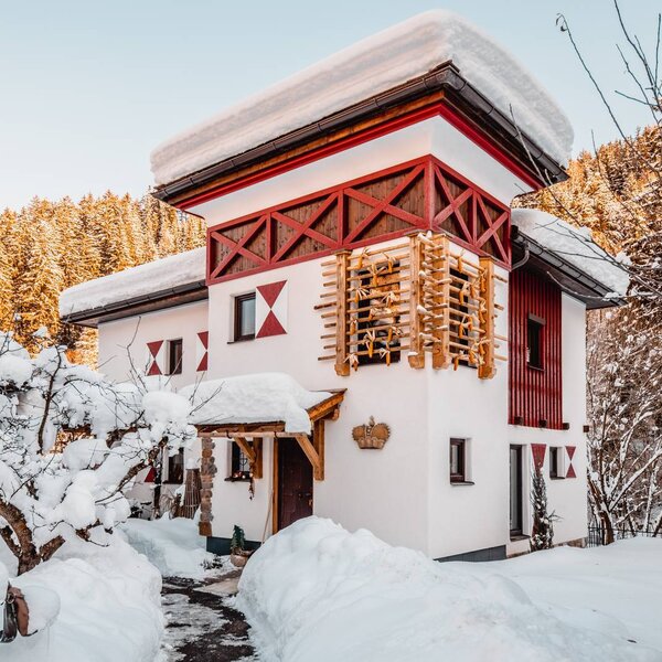 The exterior of the Farm House in winter, featuring its red and white design with distinctive wooden facade elements, surrounded by snow-covered grounds and trees.