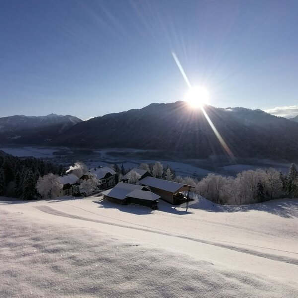 Winter view of the snowy Drautal valley and surrounding mountains from the Farm House, featuring scattered buildings and bright sunshine.