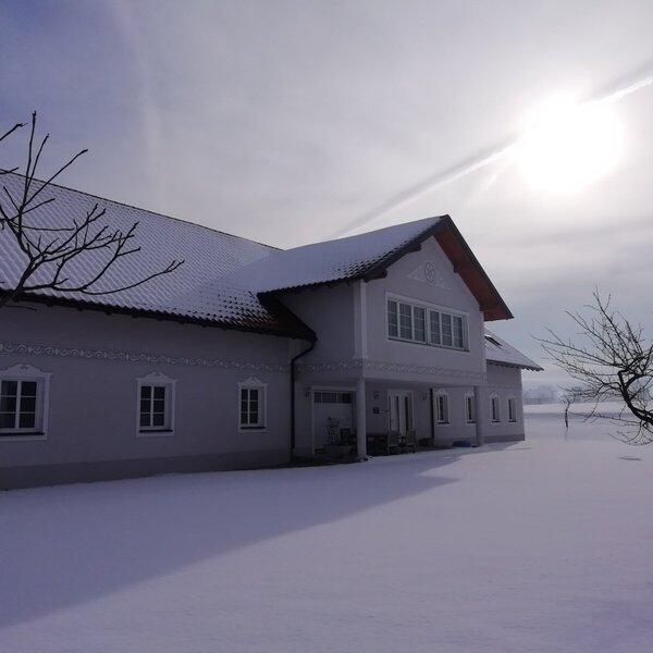 Der Bauernhof im Winter, mit schneebedecktem Dach und verschneiter Umgebung.