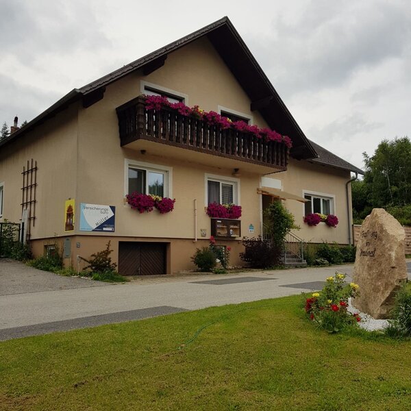 Der Bauernhof von außen mit Balkon, Fensterblumenkästen und Rasenfläche.
