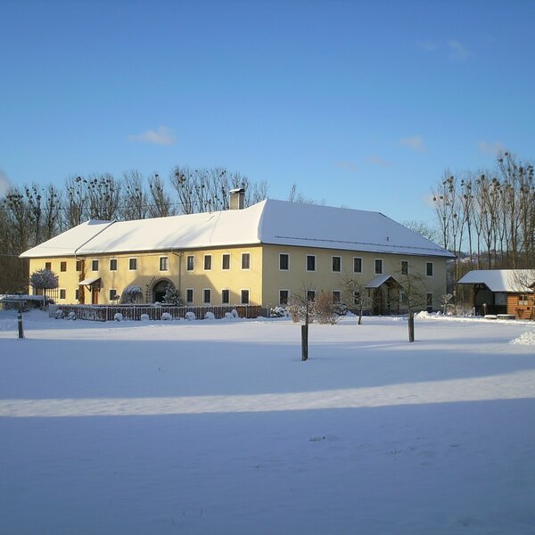 Das Hauptgebäude des Bauernhofs mit schneebedecktem Dach in einer verschneiten Winterlandschaft.