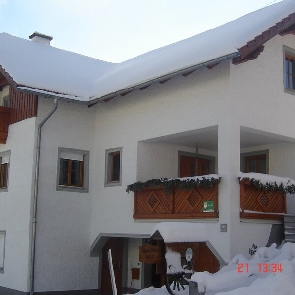Außenansicht des Bauernhofs im Winter, mit verschneiten Dächern und Balkonen.
