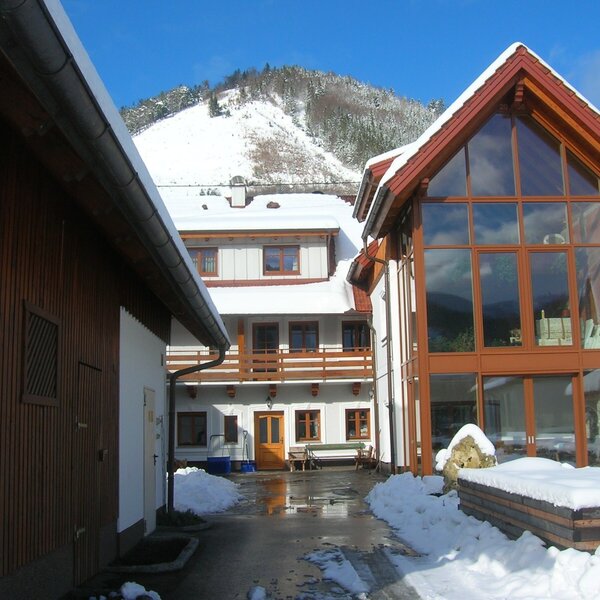The Farm House exterior in winter, featuring buildings with balconies, a large glass facade, and a snow-covered mountain view.