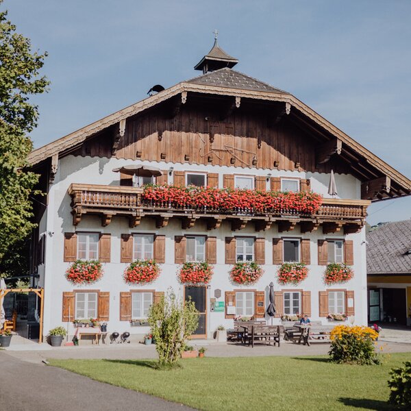 Der Bauernhof mit traditioneller Architektur, Holzbalkonen, Blumenkästen und einem Sitzbereich im Freien.