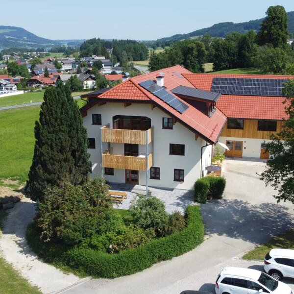 The Farm House features multiple wooden balconies, solar panels on its roof, an outdoor patio with seating, and offers views of the lake and village.