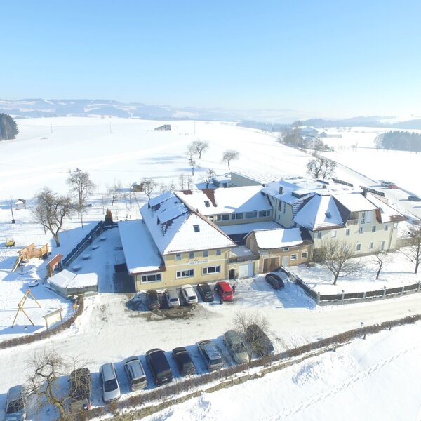 The farm house and its parking areas are surrounded by snow-covered fields, with an outdoor playground visible in the foreground.