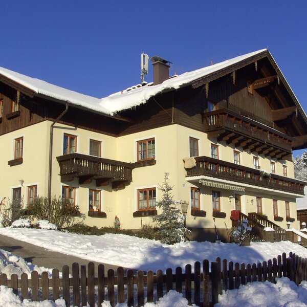 Der Bauernhof im Winter, mit traditioneller Bauweise, Holzbalkonen und schneebedecktem Gelände.