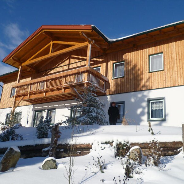 The multi-level farm house exterior displays a wooden balcony and facade, with the property surrounded by snow.