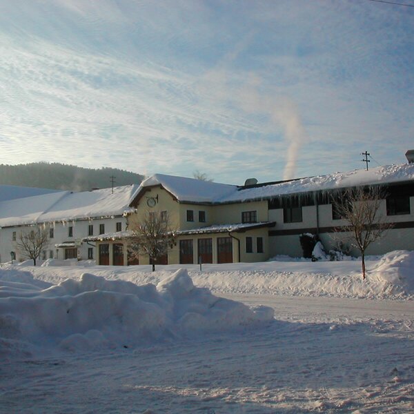 Die Außenansicht des Bauernhofs im Winter, mit schneebedeckten Dächern und Eiszapfen.