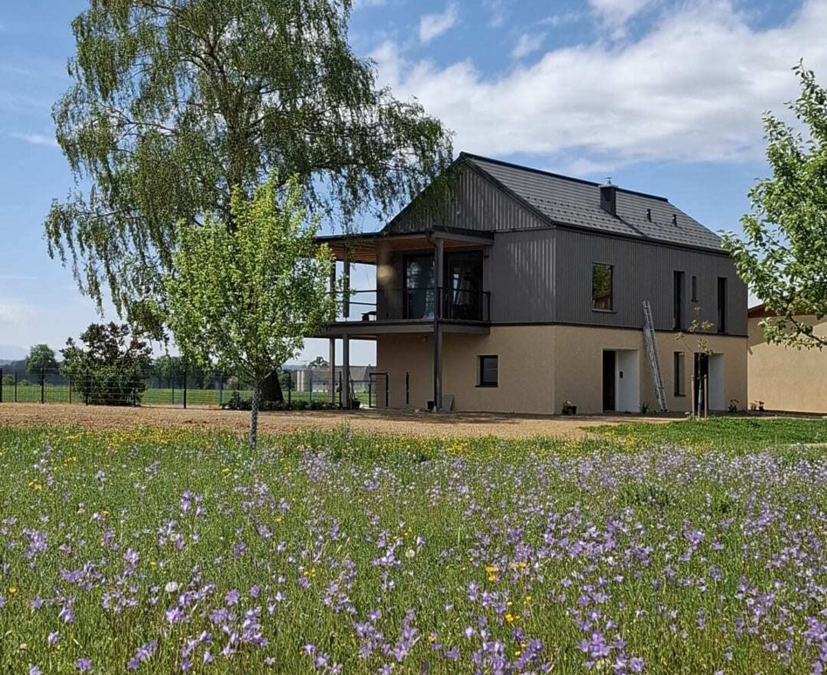 Das moderne Ferienhaus mit Balkon, umgeben von einer Blumenwiese und einem großen Baum. | © Urlaub am Bauernhof Oberösterreich / Zauner