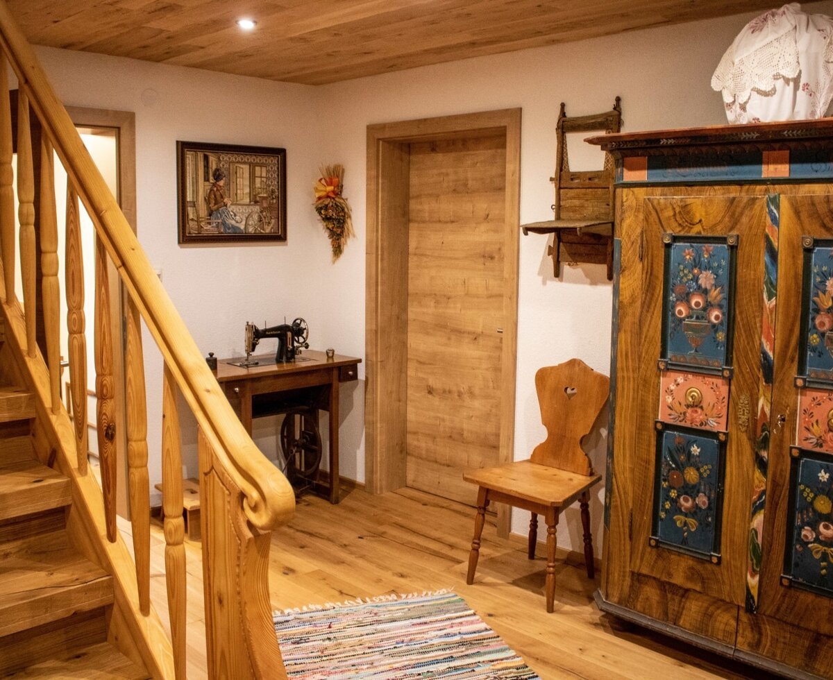 Der Eingangsbereich des Bauernhofs mit Holztreppe, traditionellem Bauernschrank und alter Nähmaschine.