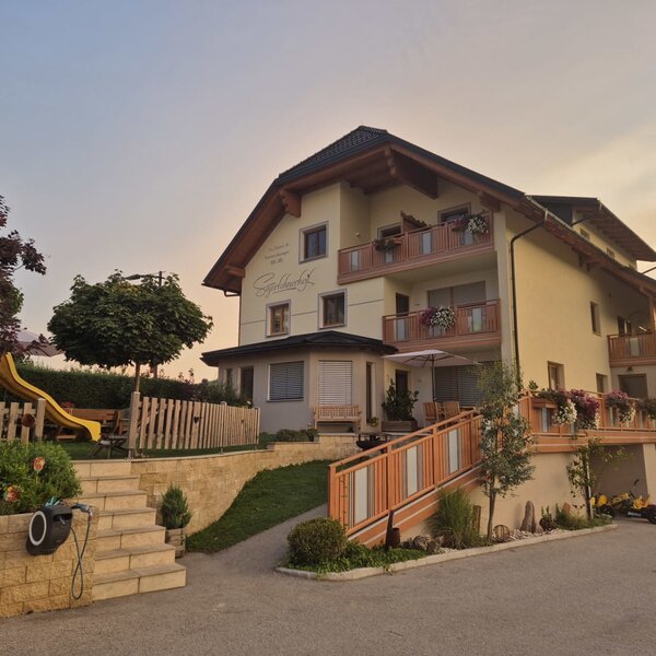 The farmhouse with balconies, a terrace with a sun umbrella, and a children's playground with a slide.