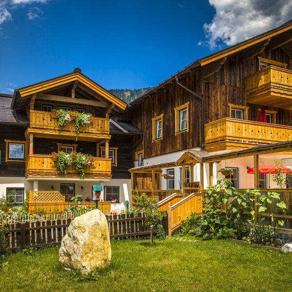 The Farm House features a traditional wooden exterior with multiple balconies adorned with flower boxes, a covered ground-floor terrace with seating, and a front lawn.