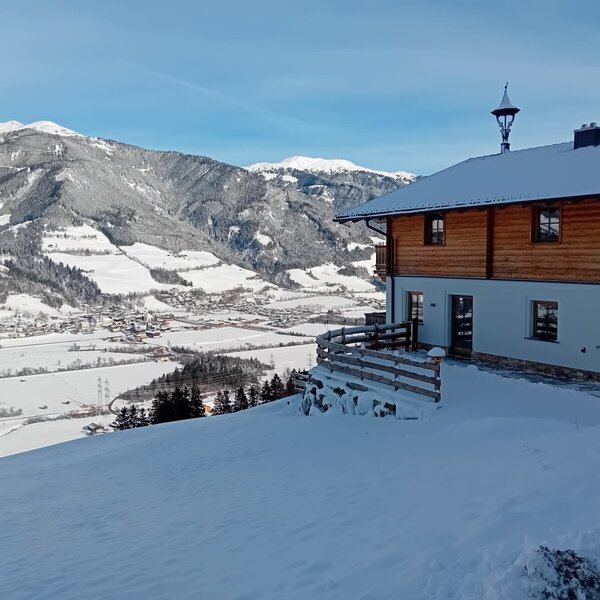 Außenansicht des Bauernhofs in winterlicher Umgebung mit Panoramablick auf das schneebedeckte Tal und die Berge.