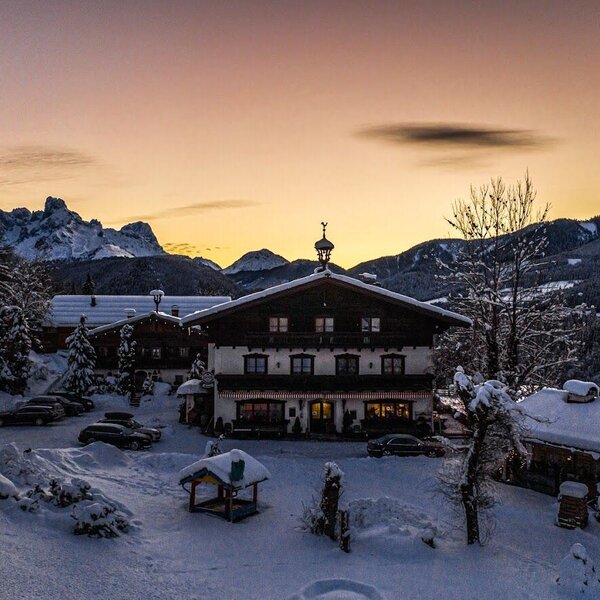 Der Bauernhof in verschneiter Winterlandschaft mit den Salzburger Dolomiten im Hintergrund bei Sonnenuntergang.