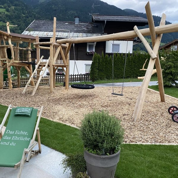 Der Spielplatz des Bauernhofs mit Holzturm, Rutsche und Schaukeln auf einem Untergrund aus Holzhackschnitzeln.