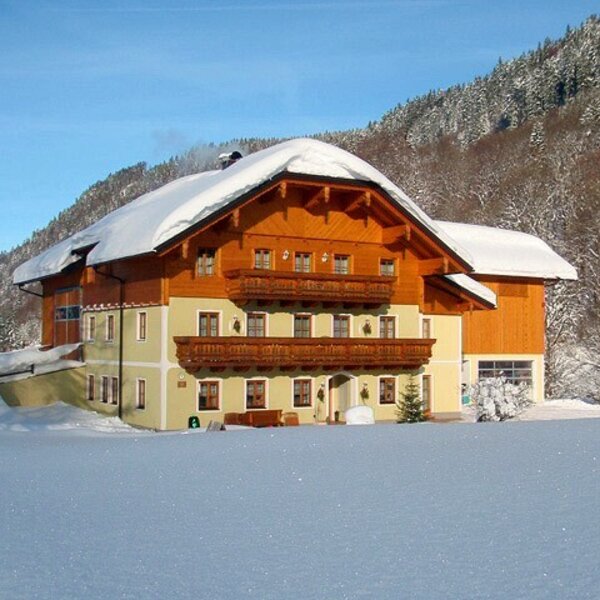 Der Bauernhof im traditionellen Stil mit Holzbalkonen im Winter, umgeben von schneebedeckten Bergen.