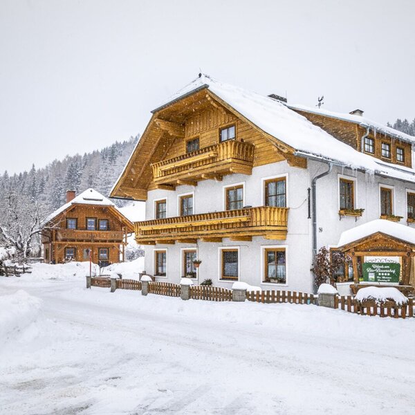 Der schneebedeckte Bauernhof Tonimörtlhof mit Holzbalkonen und dem Hinweisschild für die "4 Blumen" Auszeichnung.