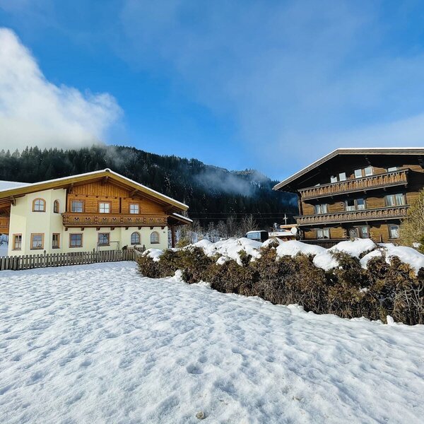 Außenansicht des Bauernhofs mit zwei traditionellen Gebäuden, die Holzbalkone aufweisen, in einer verschneiten Berglandschaft.