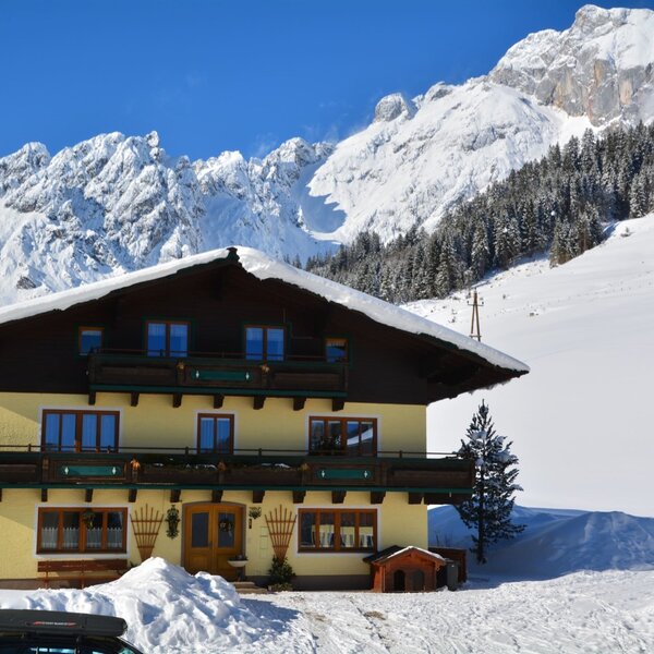 Die Außenansicht des Ferienbauernhofs mit Balkonen und schneebedecktem Dach, gelegen vor einer winterlichen Bergkulisse.